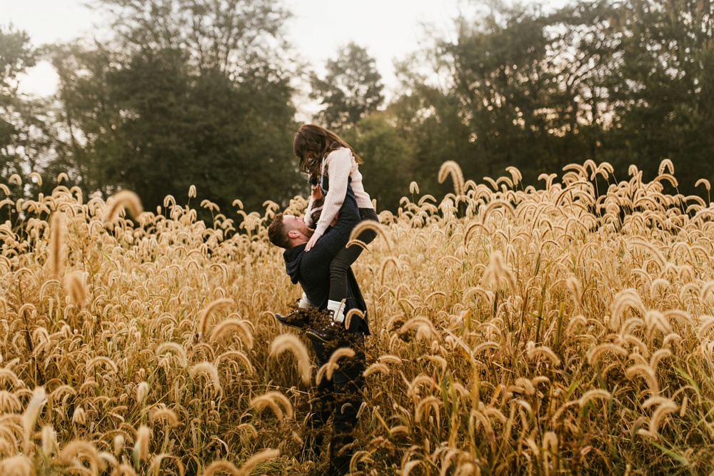 man lifting up fiance in field at auburn sunrise engagement session