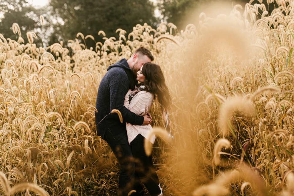 man kissing fiance in field at auburn sunrise engagement session