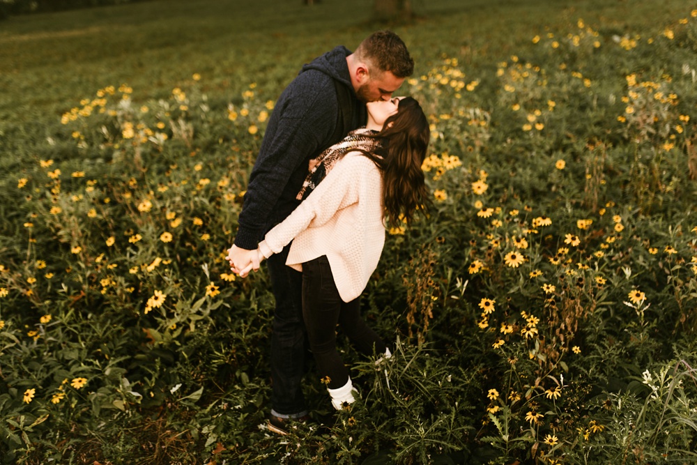 couple kissing among daisies in field at auburn sunrise engagement session