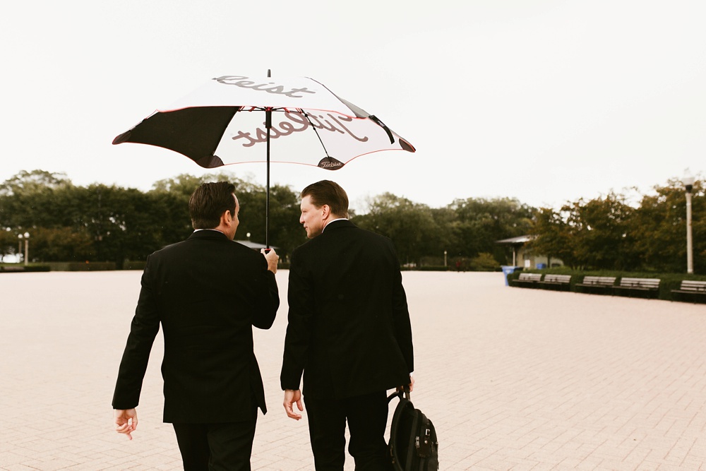 groom and best man walking under umbrella at skydeck willis tower chicago wedding