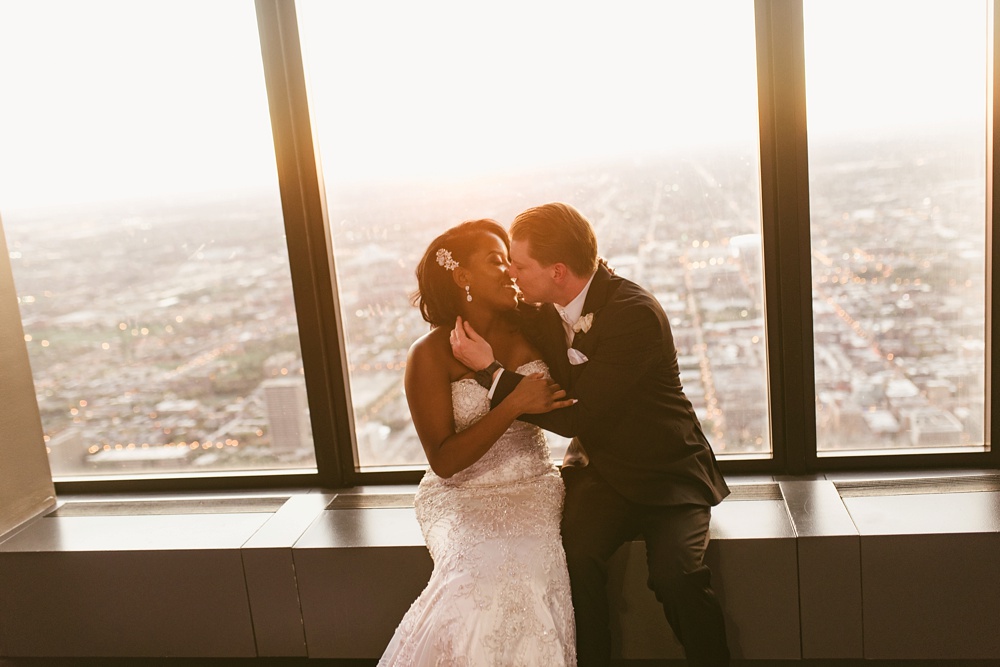 bride and groom kissing in front of window at sunset at skydeck willis tower wedding
