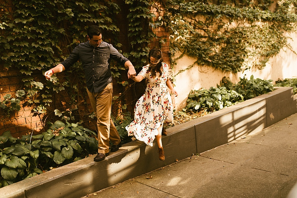 couple holding hands on ledge at downtown grand rapids engagement session