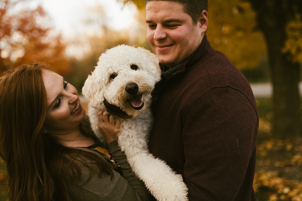 couple laughing holding dog at chain o'lakes fall engagement session