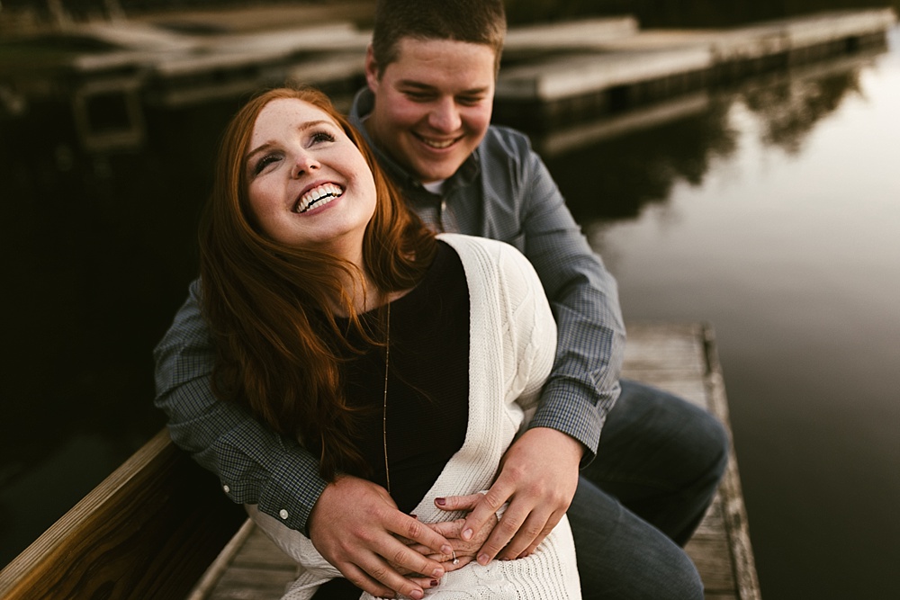 couple laughing on pier at chain o'lakes fall engagement session