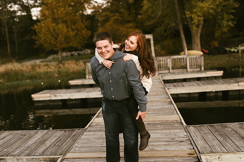 couple wrestling on pier at chain o'lakes fall engagement session