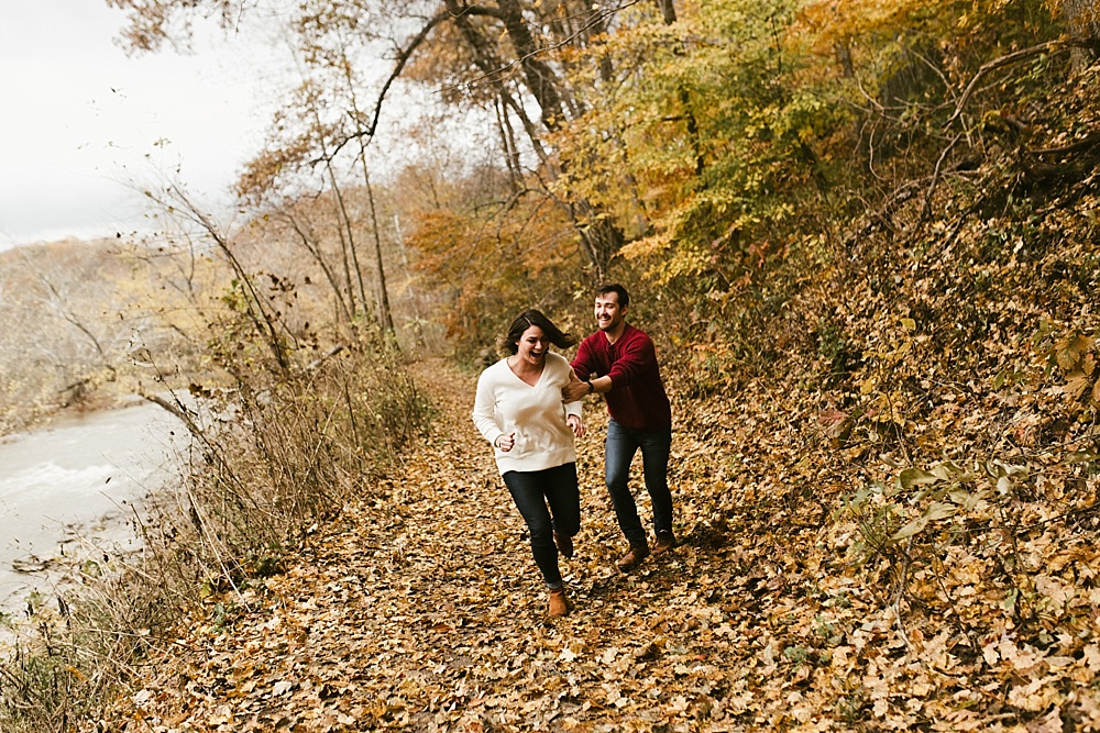 couple running and laughing through woods at cataract falls fall engagement session