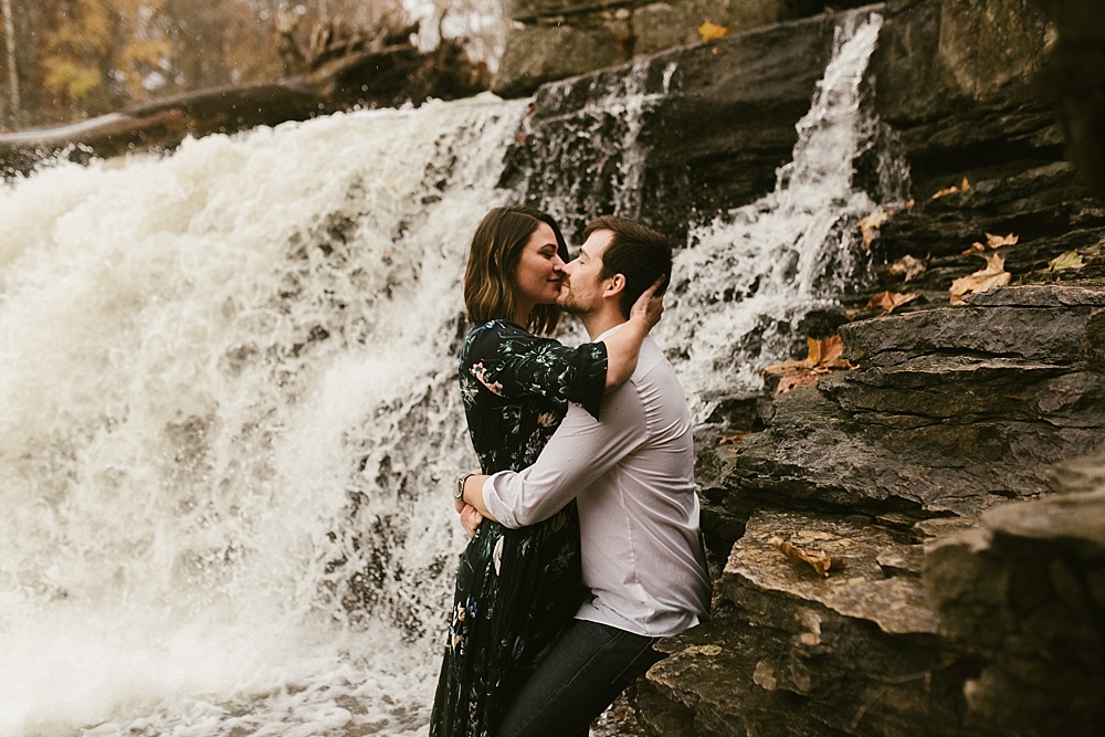 couple hugging in front of falls at cataract falls fall engagement session