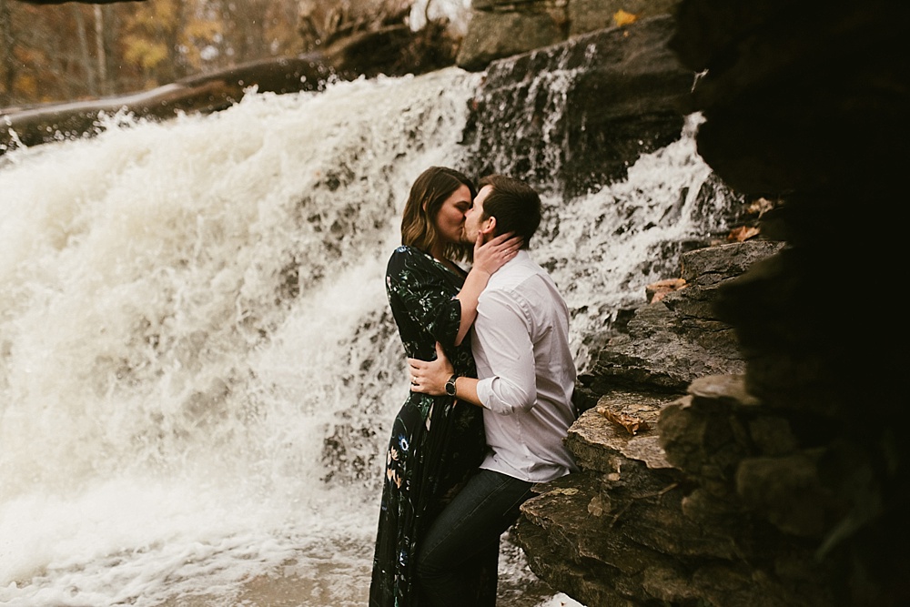 couple kissing in front of falls at cataract falls fall engagement session