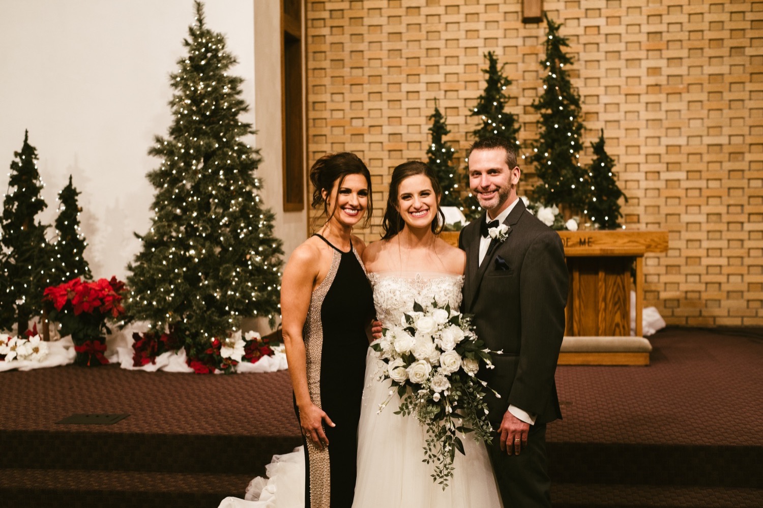 bride and parents in front of christmas trees at fort wayne winter wedding