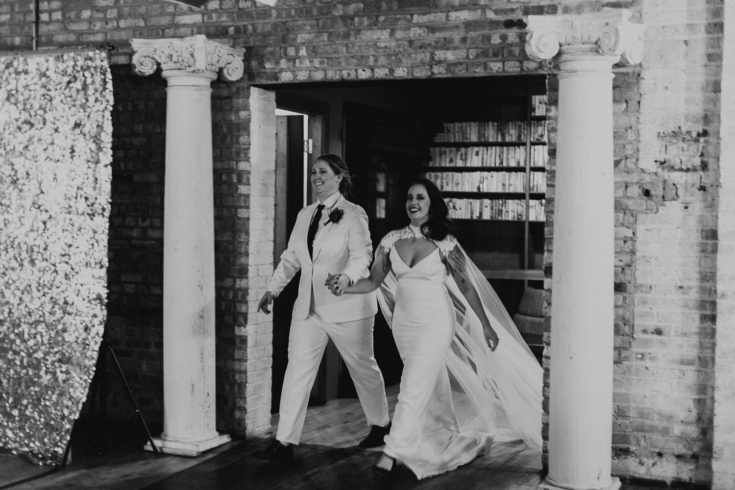 Black and white photo of bride and bride walking into wedding reception.