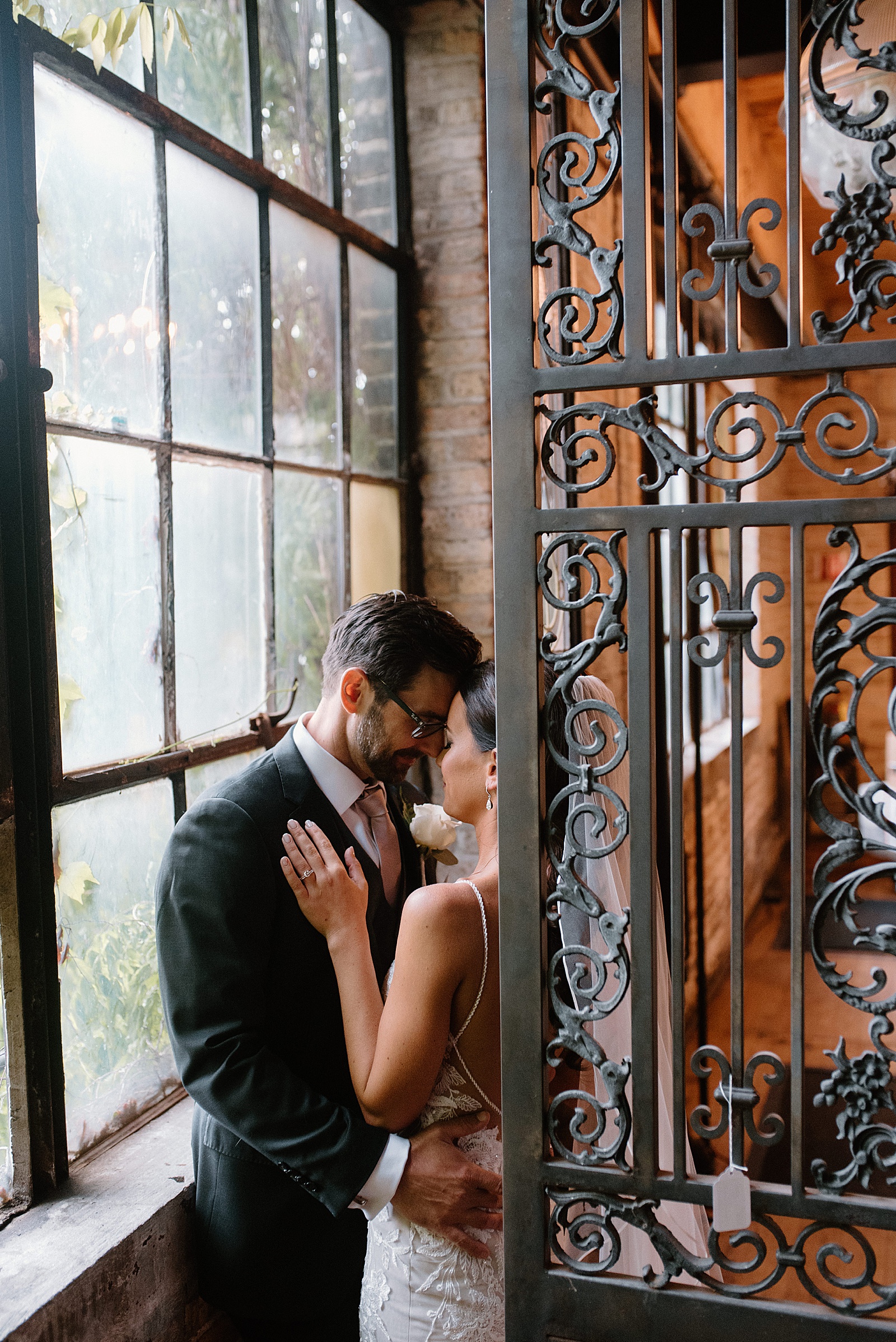 Bride and groom embracing behind an iron gate by wedding photographer, Indigo Lace. 