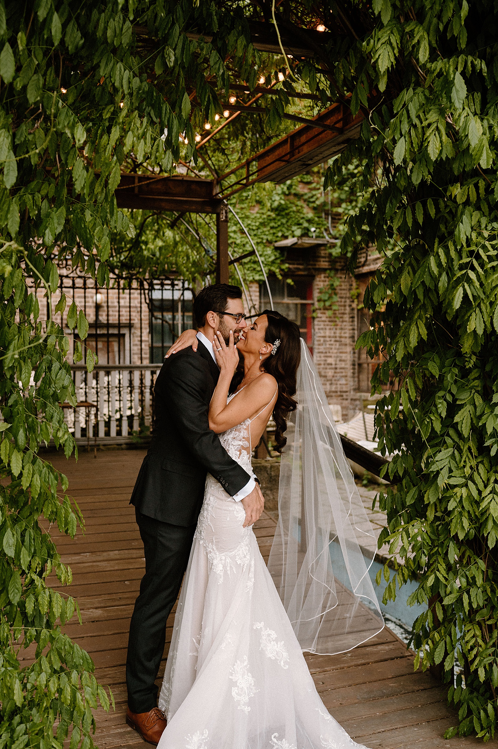 Bride and groom about to kiss under the green courtyard arch at Salvage One