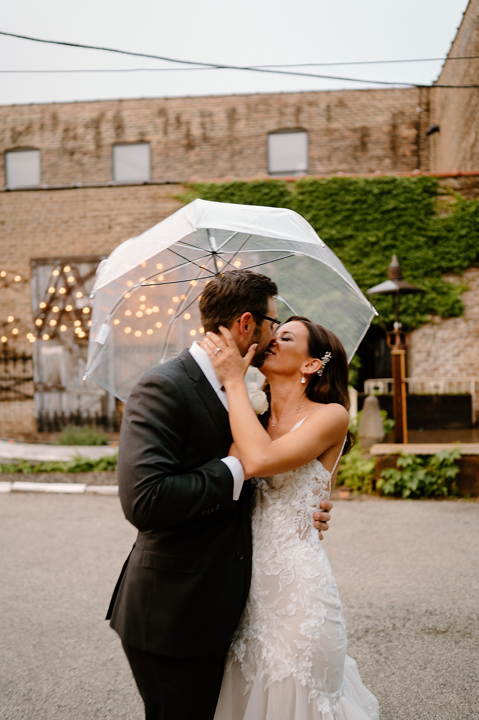 Bride and groom kiss under a clear umbrella for their rainy wedding day 