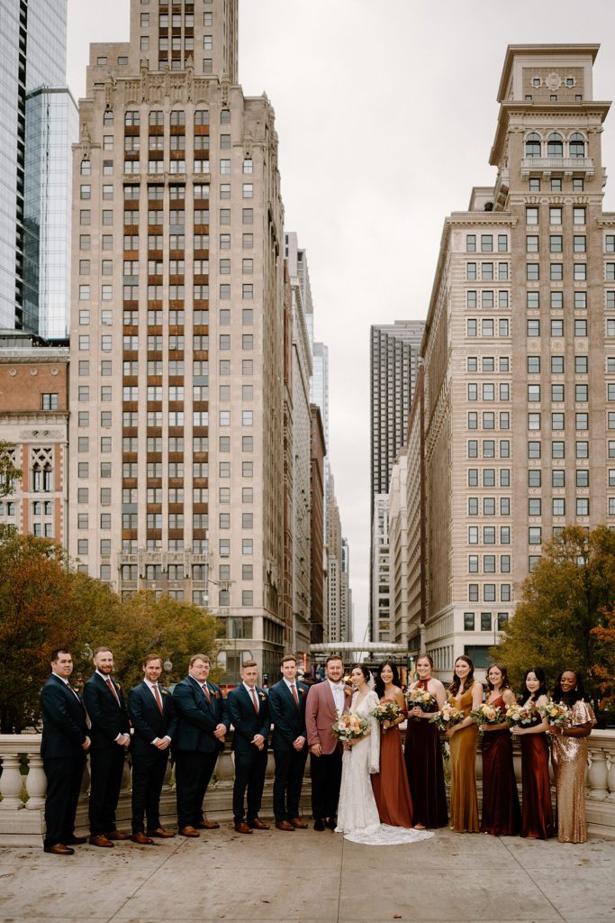 Bride and groom with their wedding party in Fall colors standing with downtown Chicago in the background.