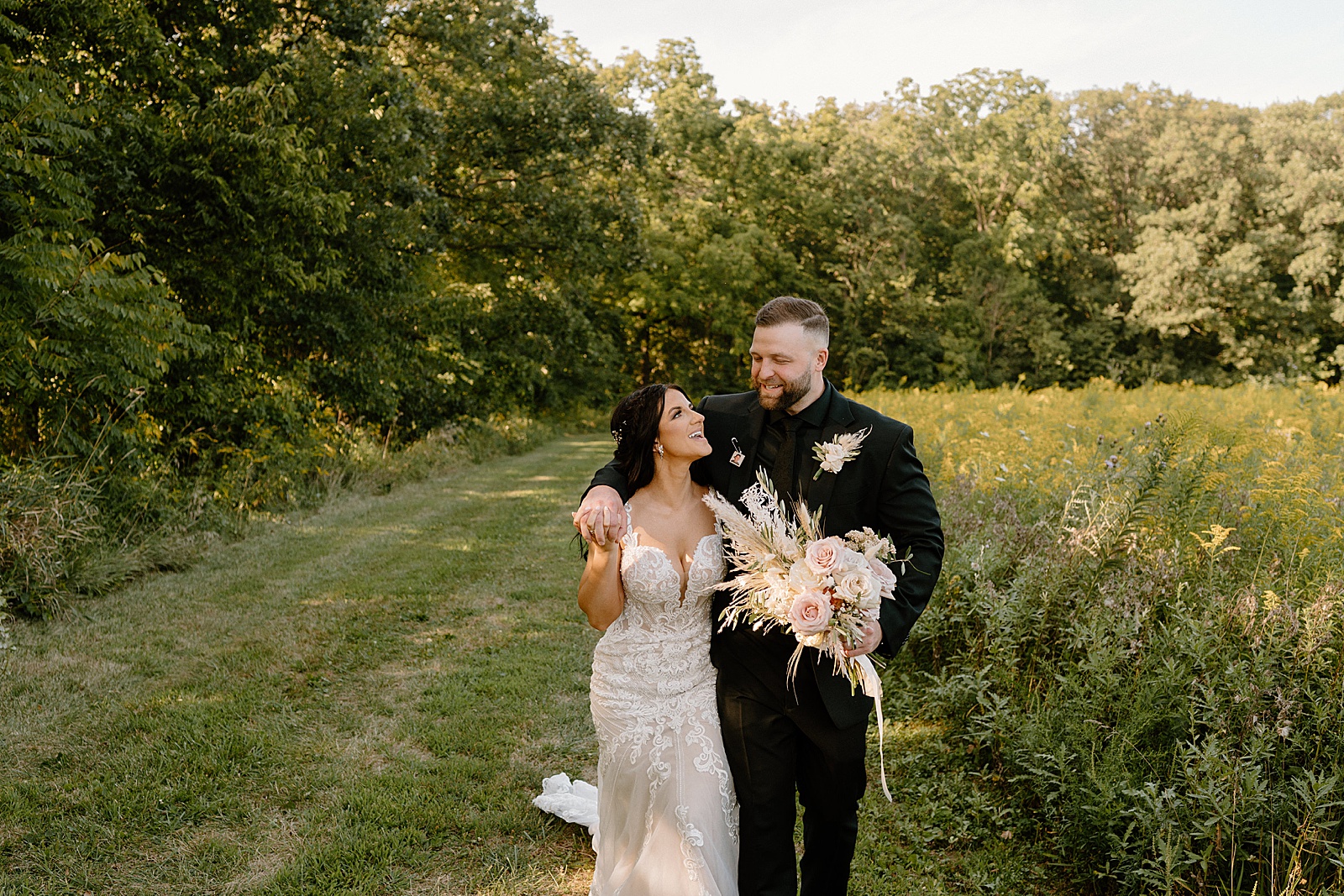 bride and groom walking through a field together for their Indiana Summer Boho wedding