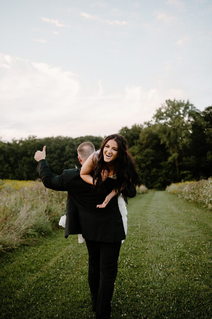 Groom throwing bride over his shoulder while she is laughing and he is holding up a 'thumbs up'. 