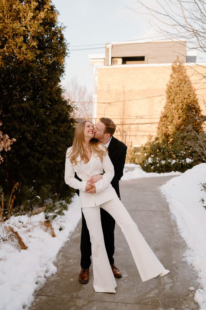 Woman in a white suit and man in black suit hugging in the snow by Chicago wedding photographer Indigo Lace