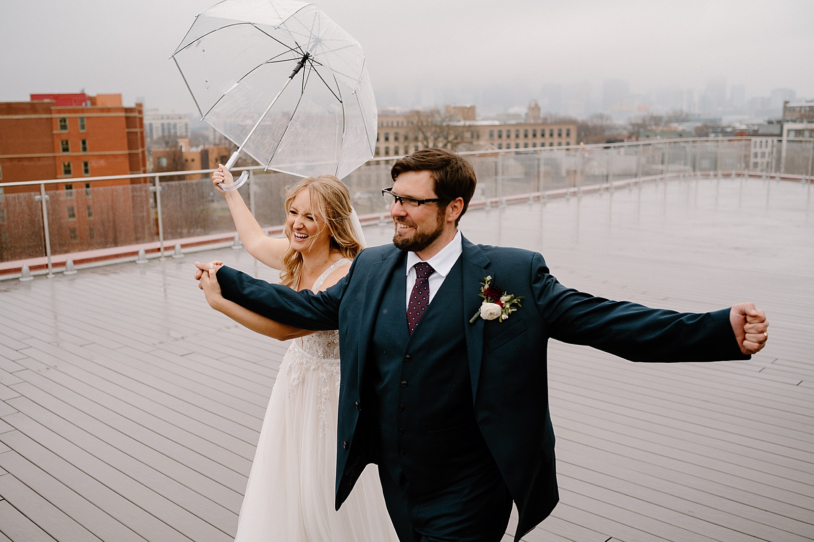 bride and groom laughing in the rain for couples portraits at their wedding 