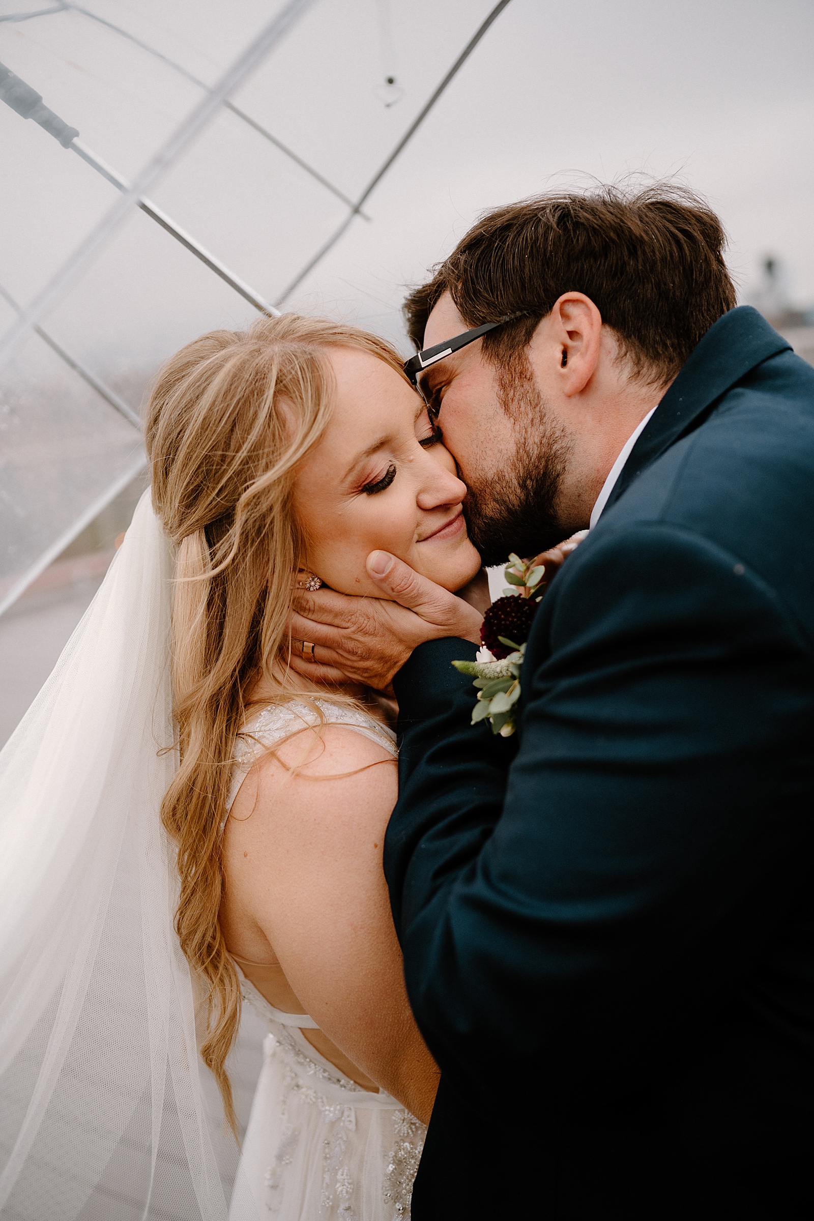 Groom kissing bride in the rain under an umbrella by Midwest wedding photographer Indigo Lace