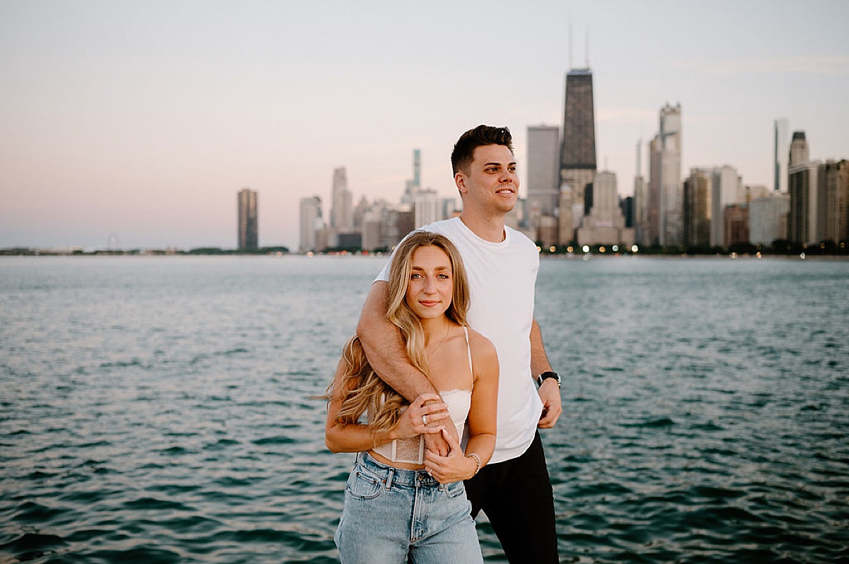 man in white shirt and black jeans poses with fiancee during Grant Park and Chicago Skyline Engagement Session