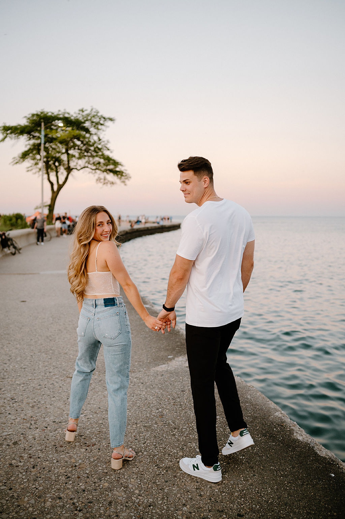 young couple walks hand in hand by the water during Grant Park and Chicago Skyline Engagement Session