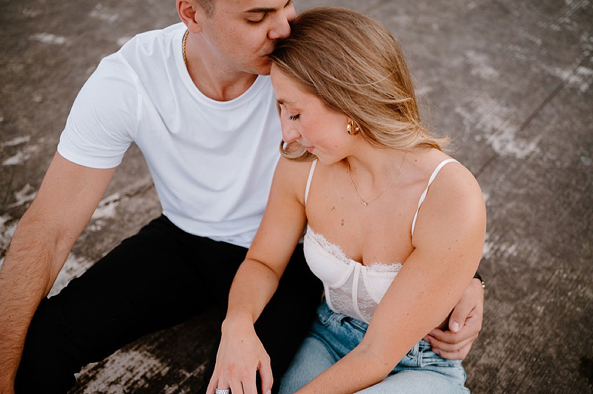 man in crisp white tee and black jeans kisses fiancee's forehead during engagement shoot by midwest wedding photographer