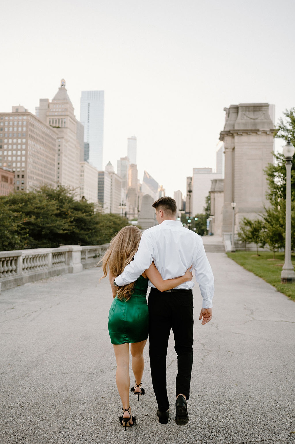 couple in green dress and white dress shirt walk arm in arm through grant park during shoot by midwest wedding photographer