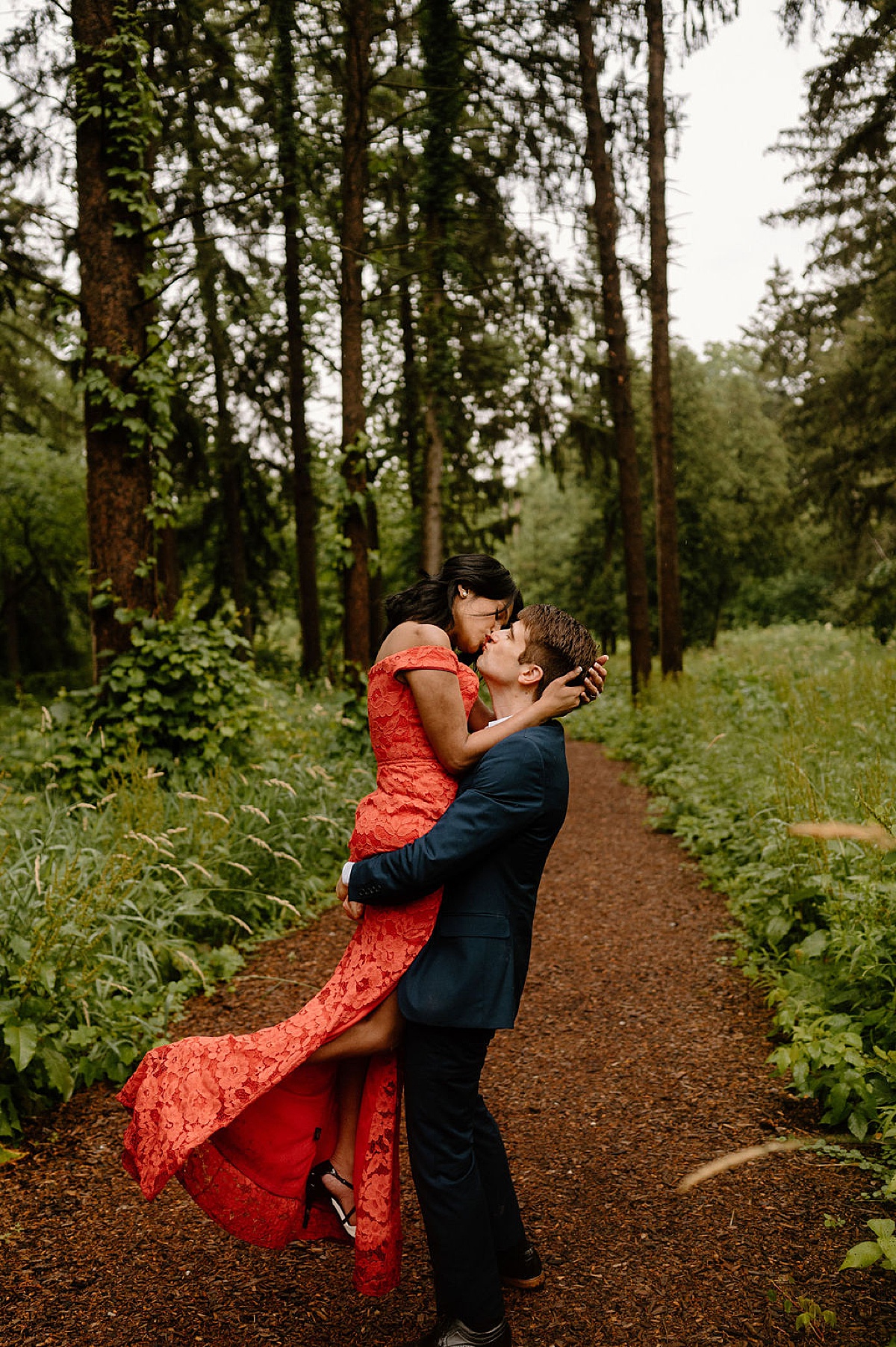 man sweeps fiancee off her feet while wearing long red gown during shoot by Indigo Lace Collective