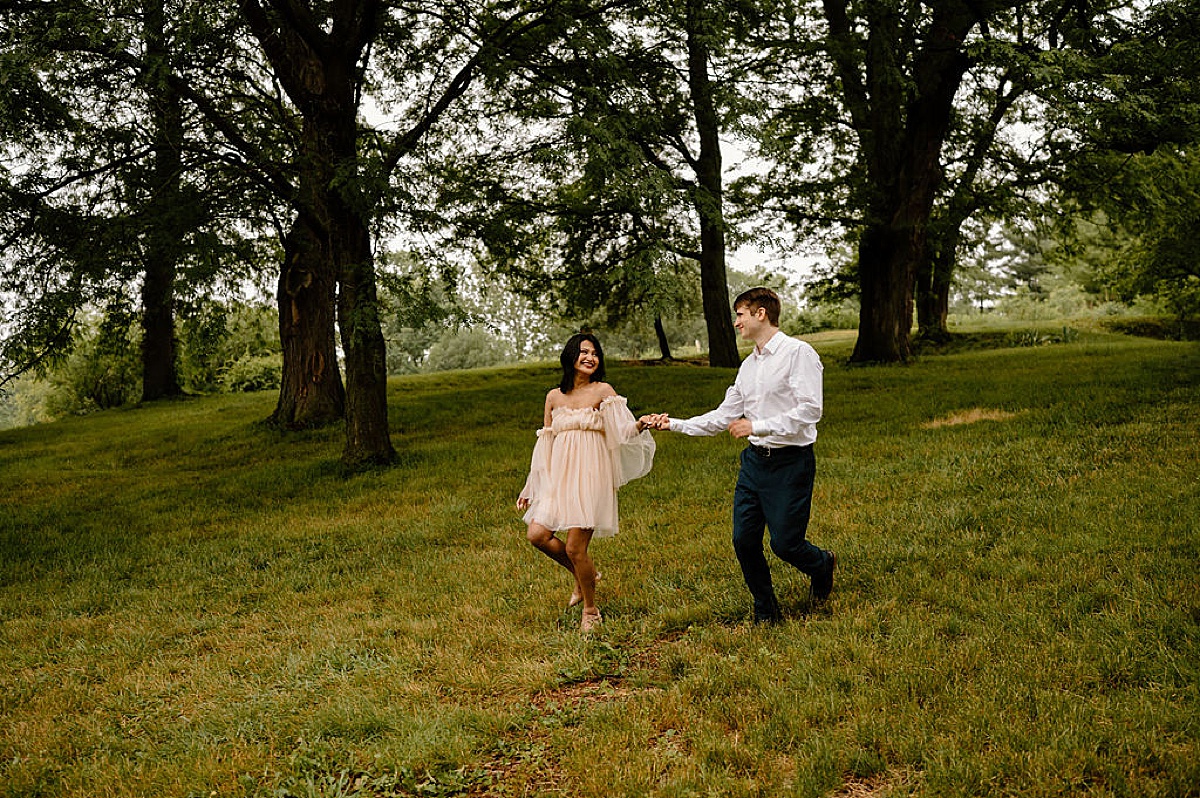 man and woman frolic through a field during engagement shoot by Indigo Lace Collective