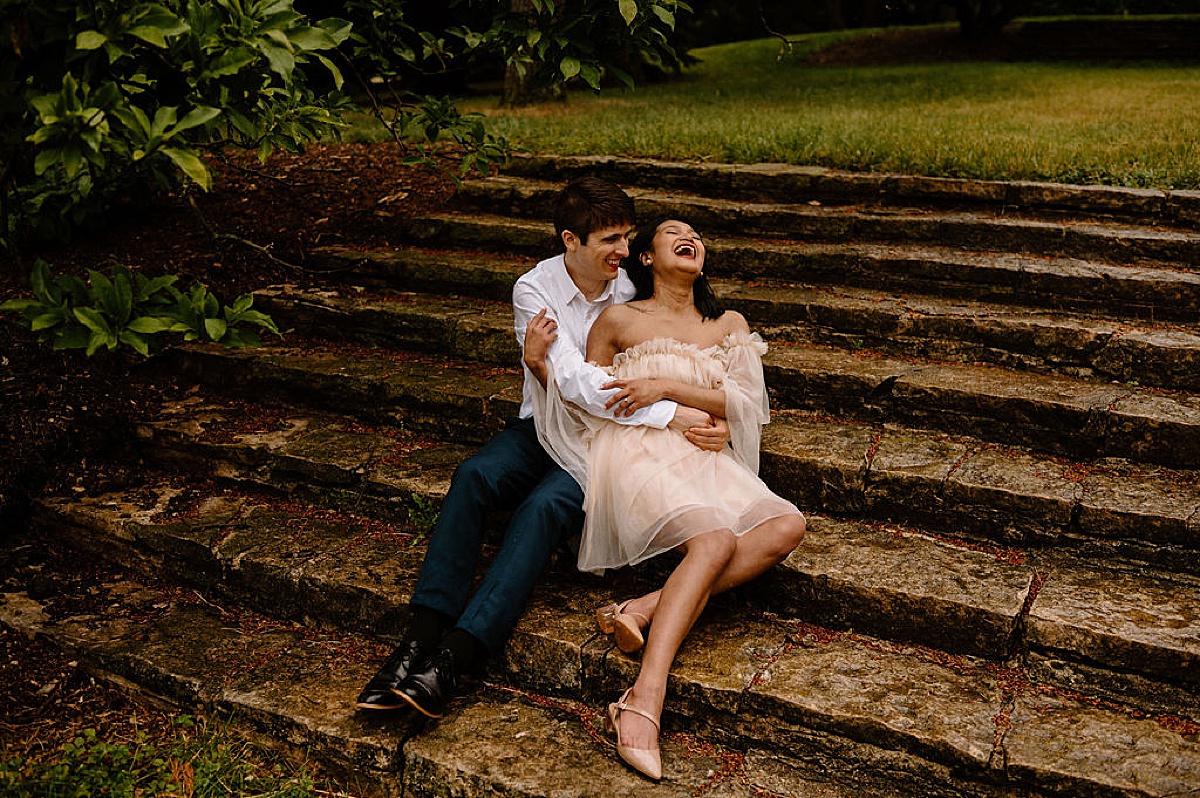 couple laugh while posing on steps during romantic shoot by midwest wedding photographer