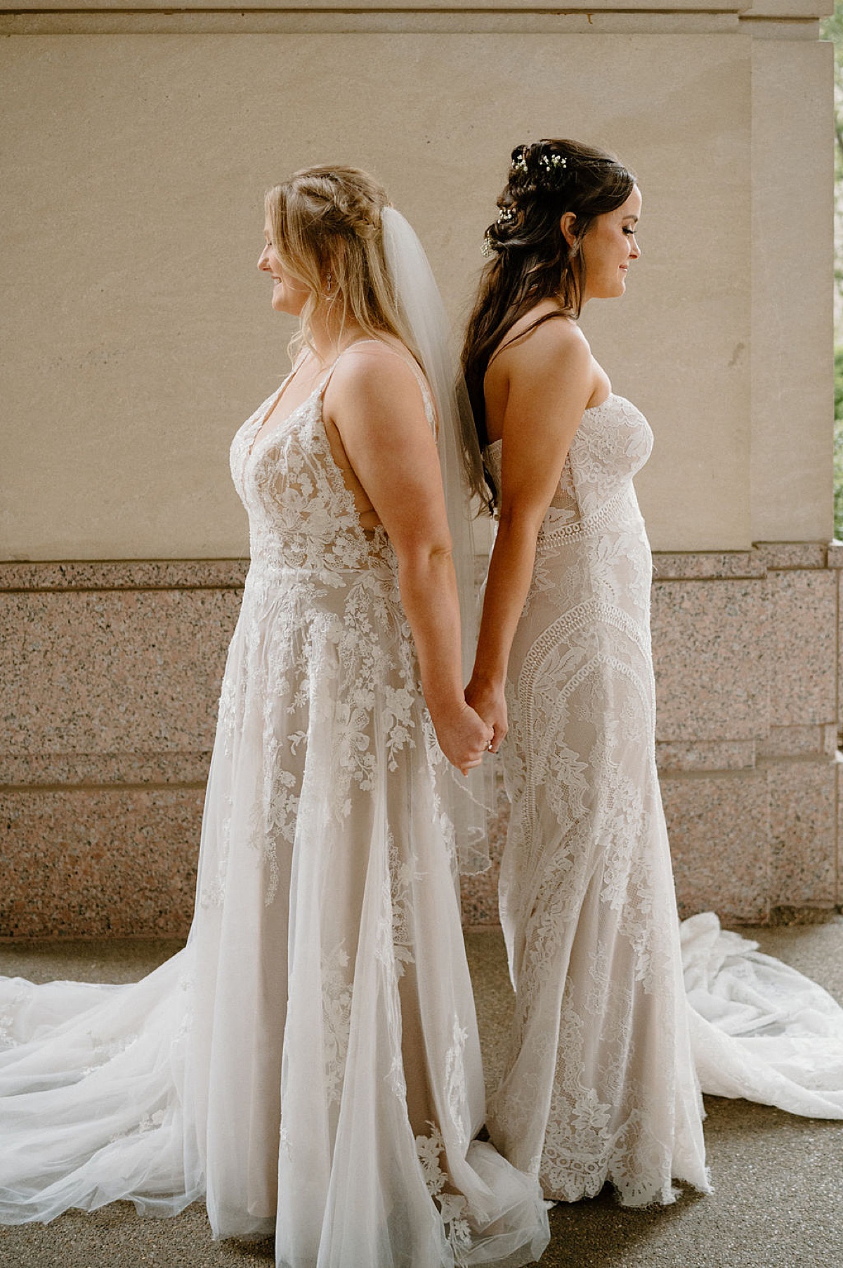 Two brides in lace gowns stand back to back before same sex wedding at BASH Indianapolis