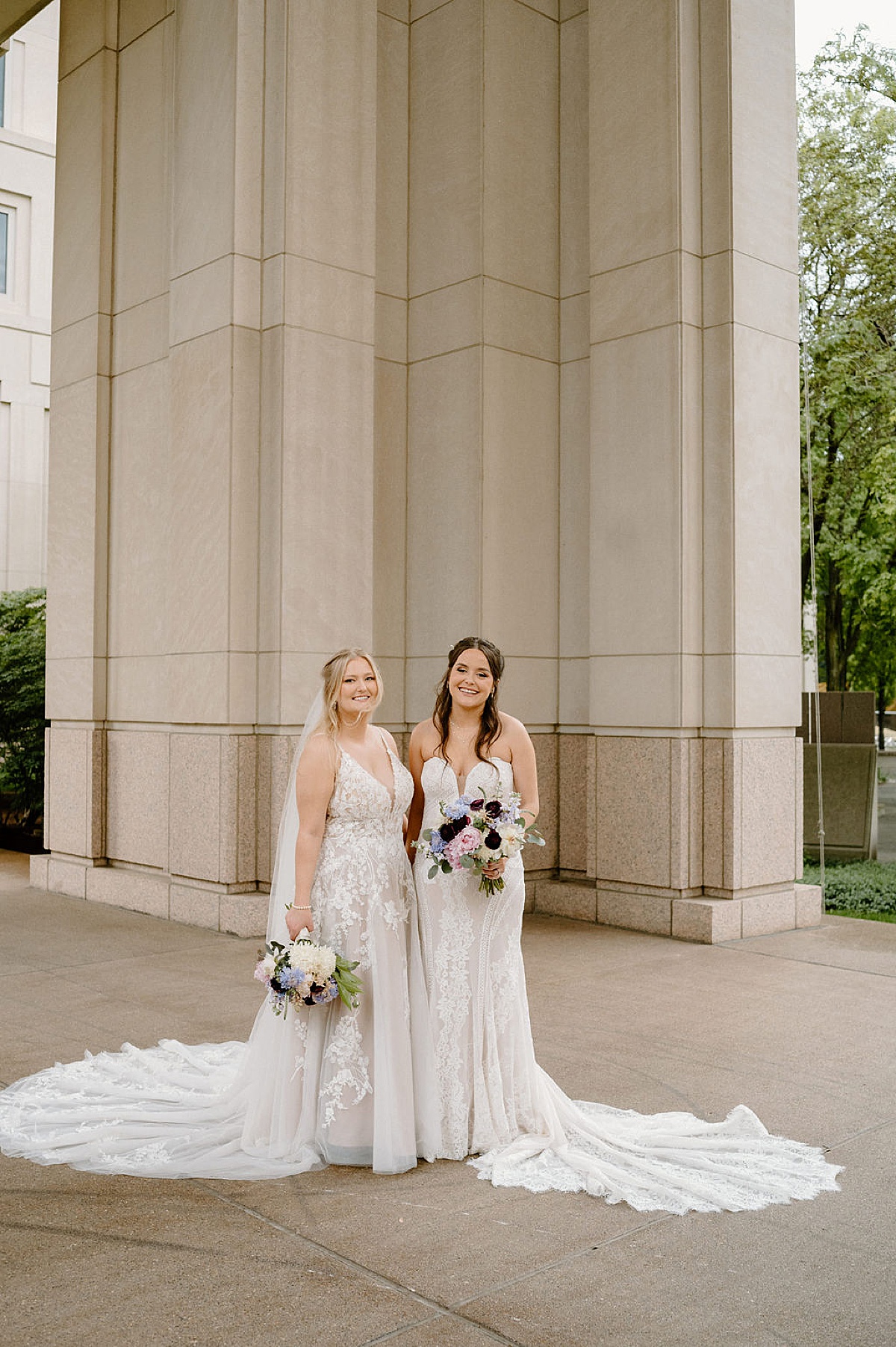 Two brides in lace and chiffon gowns pose with bouquets before same sex wedding at BASH Indianapolis