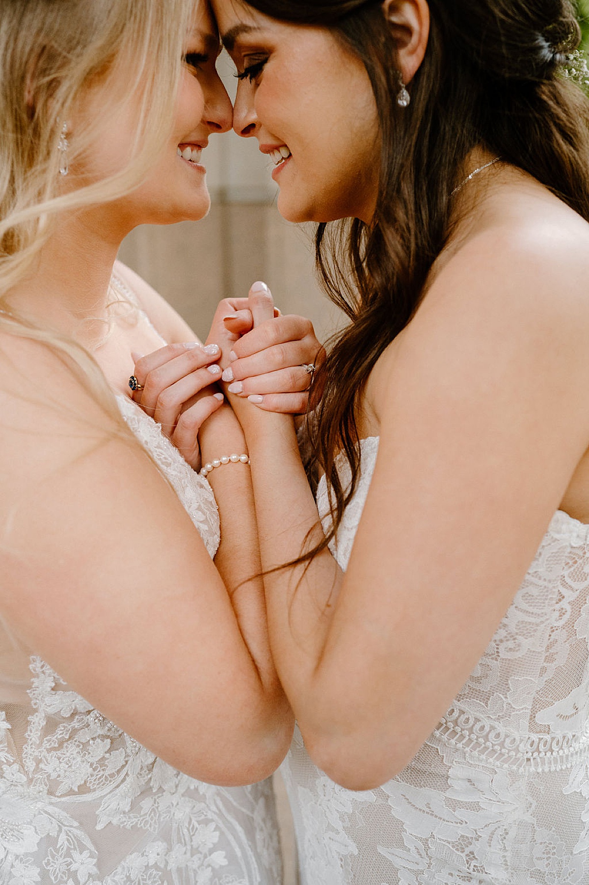 Two brides with diamond earrings and rings lean together and smile before same sex wedding at BASH Indianapolis