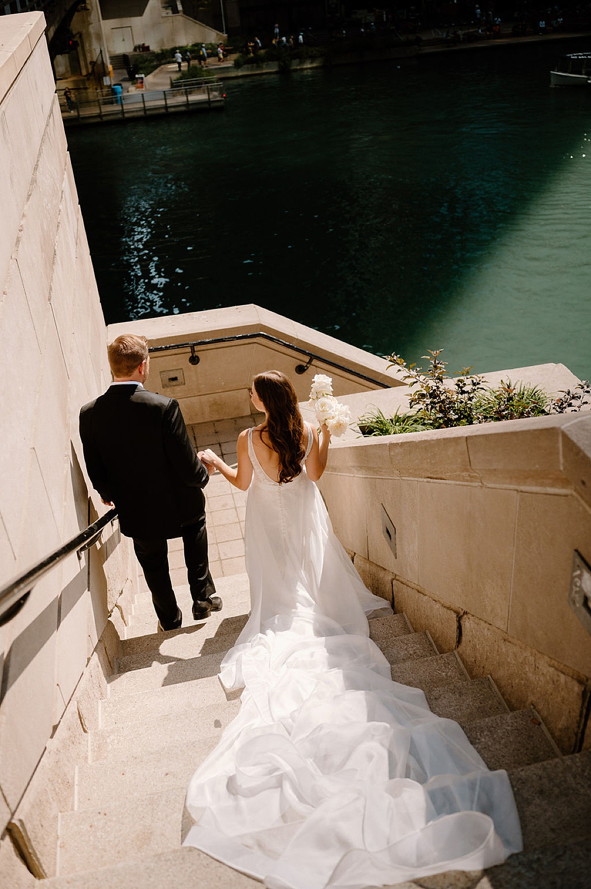 bride and groom walk down stone steps to chicago waterfront during elegant editorial wedding at bridgeport art center
