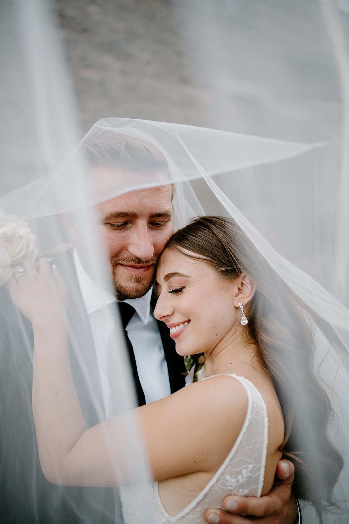 bride and groom embrace under wedding veil during shoot by midwest wedding photographer