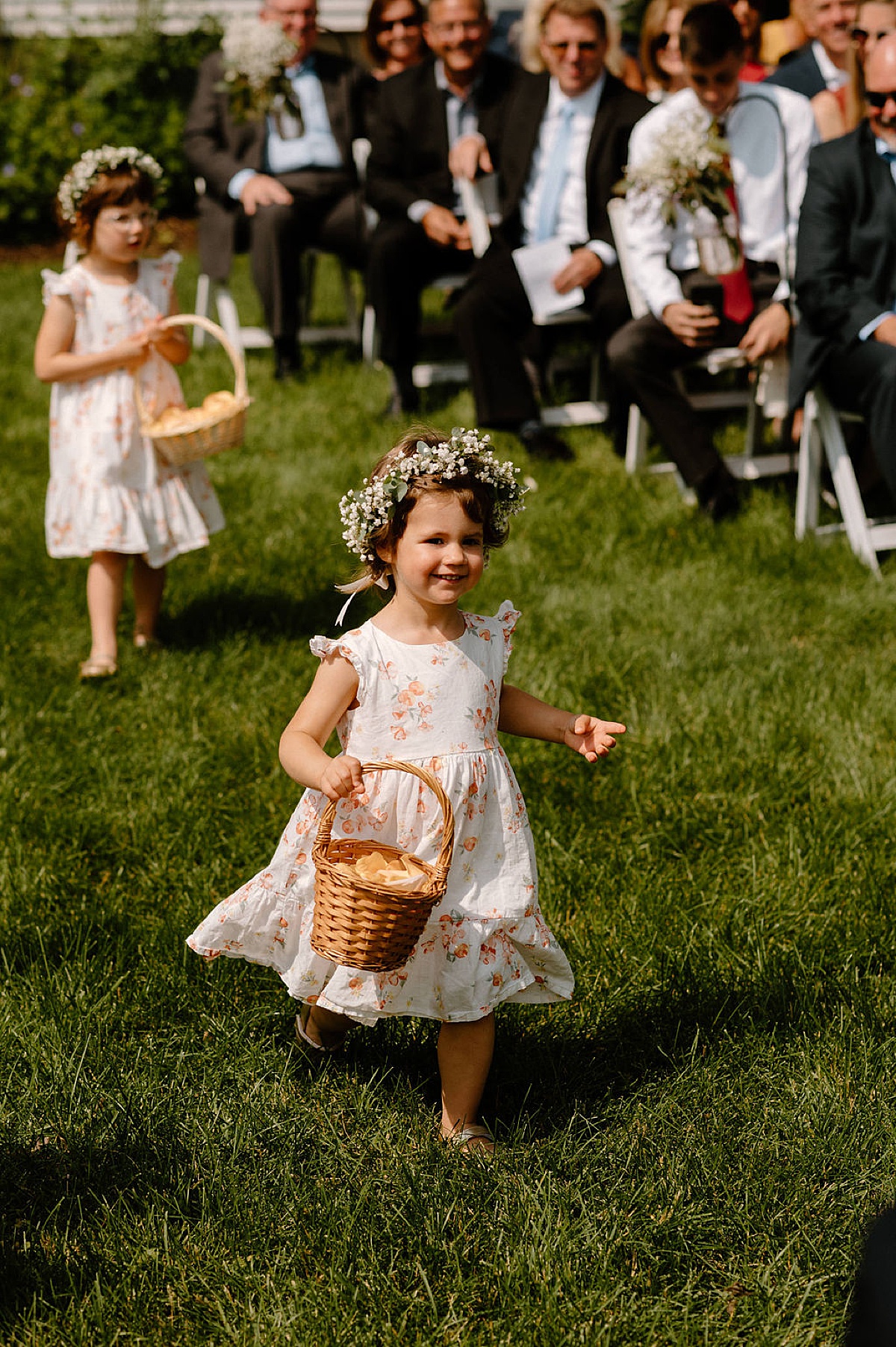 flower girls in floral sundresses and baby's breath flower crowns frolic down the aisle during ceremony shot by indigo lace collective