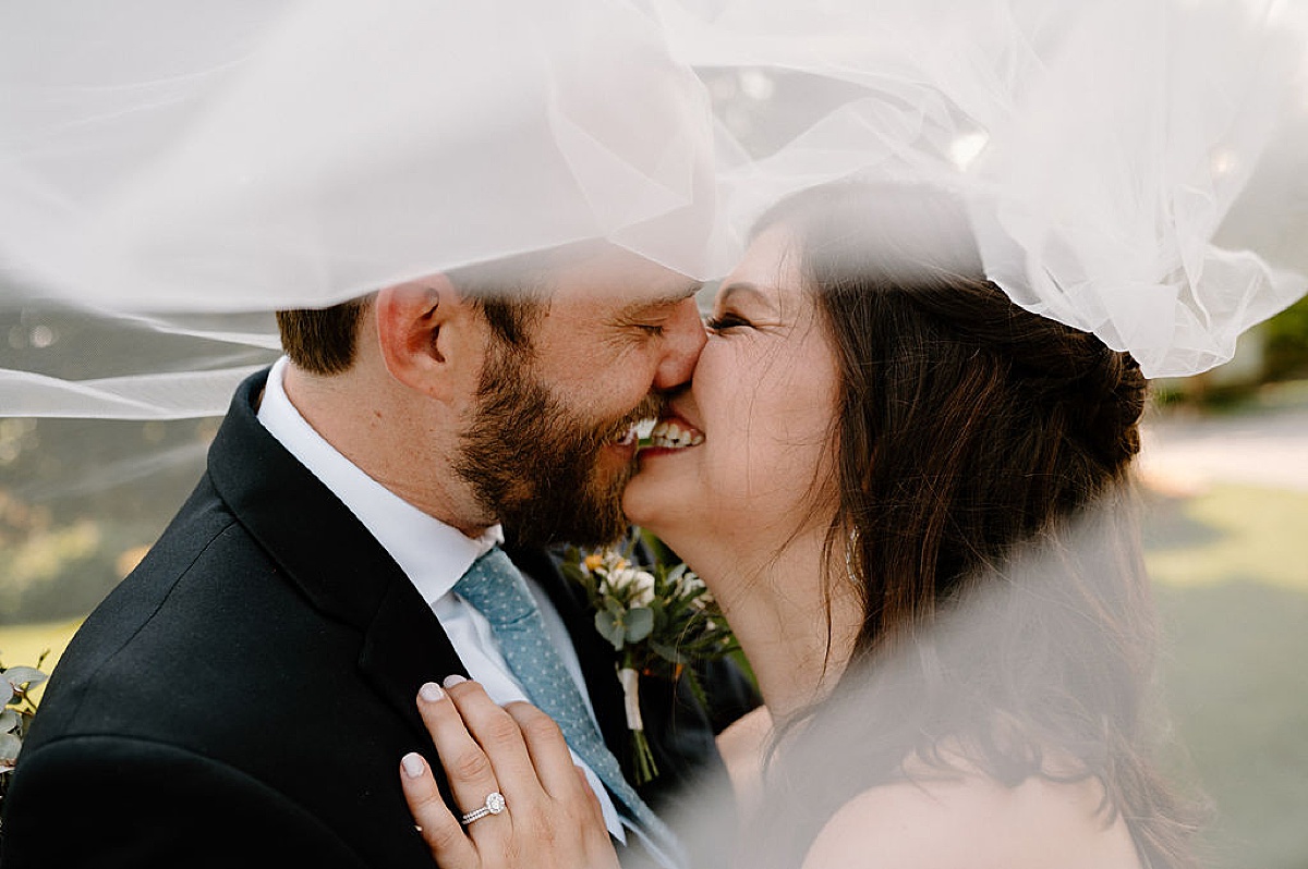 bride and groom kiss under veil after rustic farm ceremony shot by midwest wedding photographer