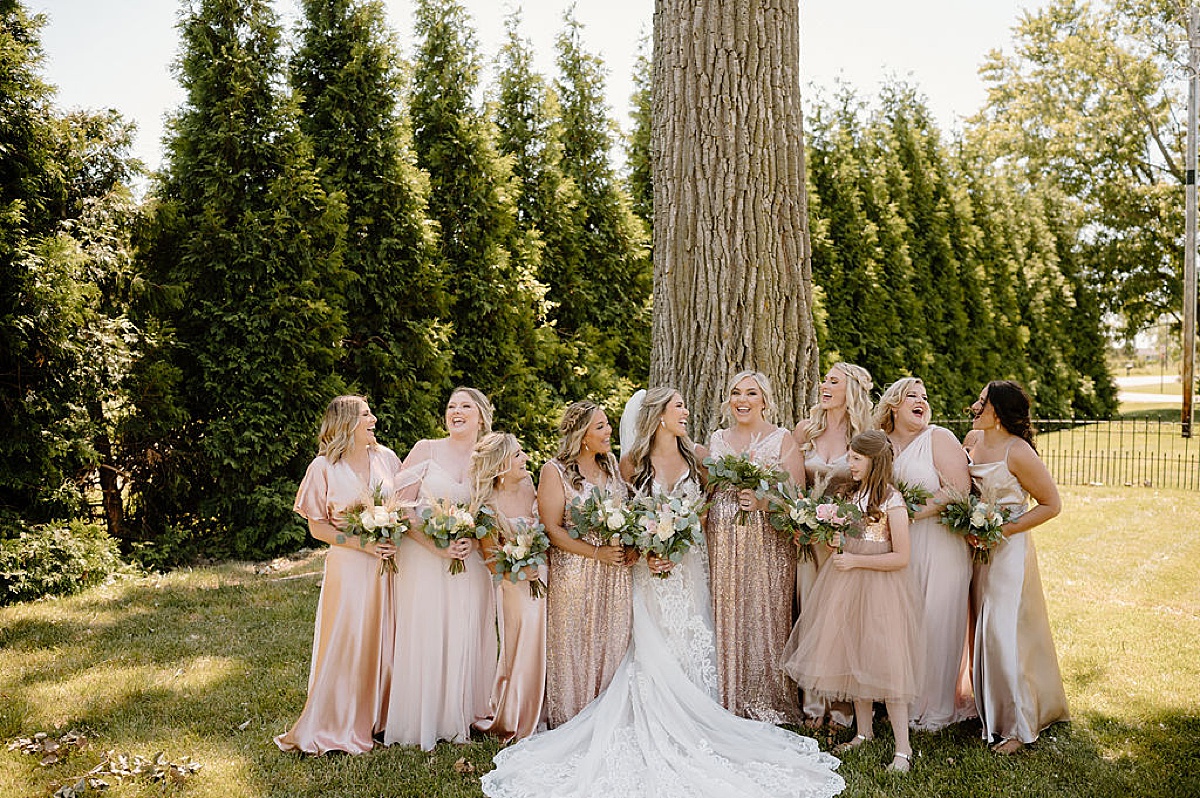 bridal party in pink satin and sequin dresses laugh and pose with bride before good vibes summer wedding at union 12