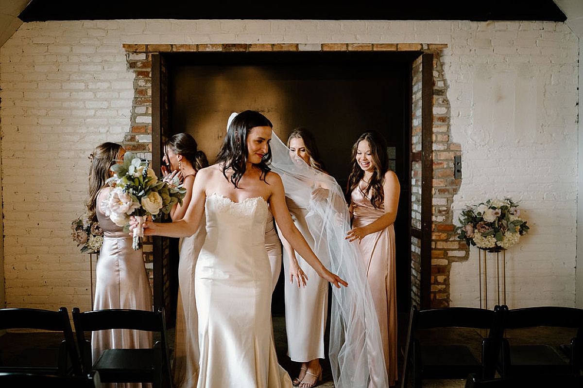 bridesmaids in champagne satin dresses help bride get ready before Heartfelt Paper Mill on the Landing Wedding