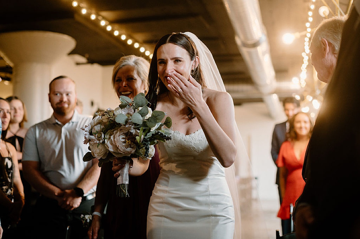 bride cries happy tears on seeing groom at the end of the aisle during ceremony shot by midwest wedding photographer