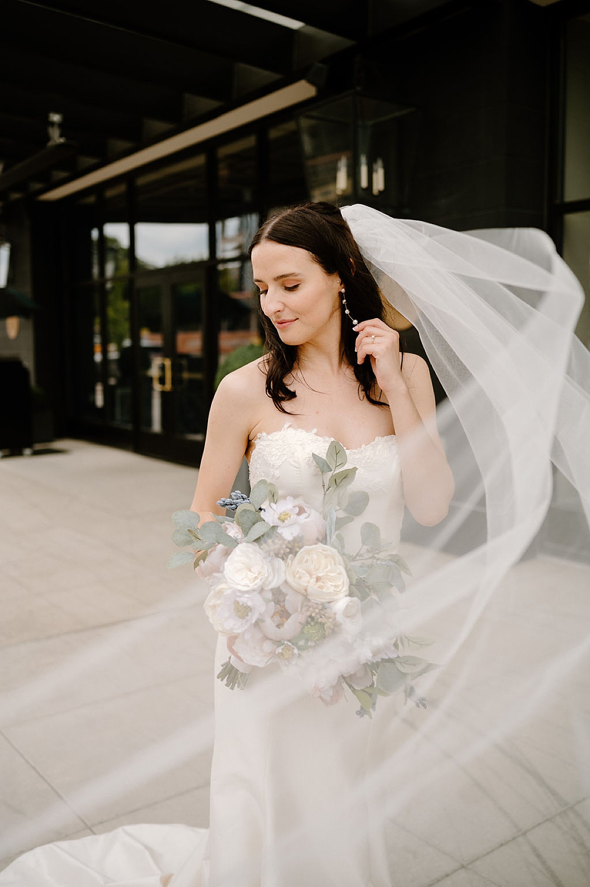 bride in elegant shift wedding gown with white bouquet poses on elegant street during shoot by Indigo Lace Collective