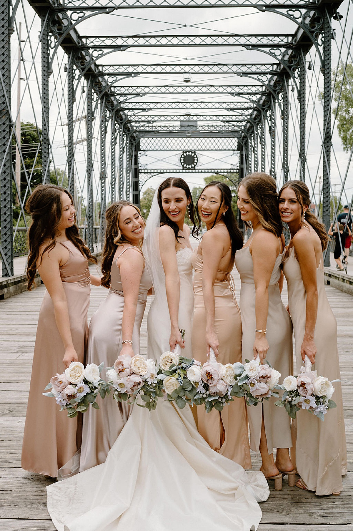 bridesmaids in champagne satin dresses pose with elegant bride holding white bouquets during shoot by Indigo Lace Collective