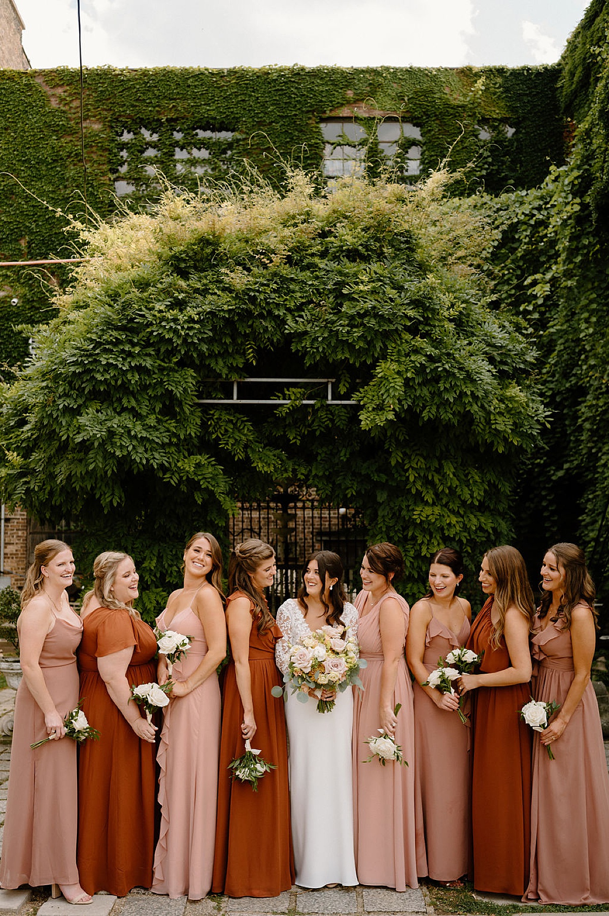 bridal party in peach and rust color chiffon dresses surround bride in white lace before Salvage one summer wedding