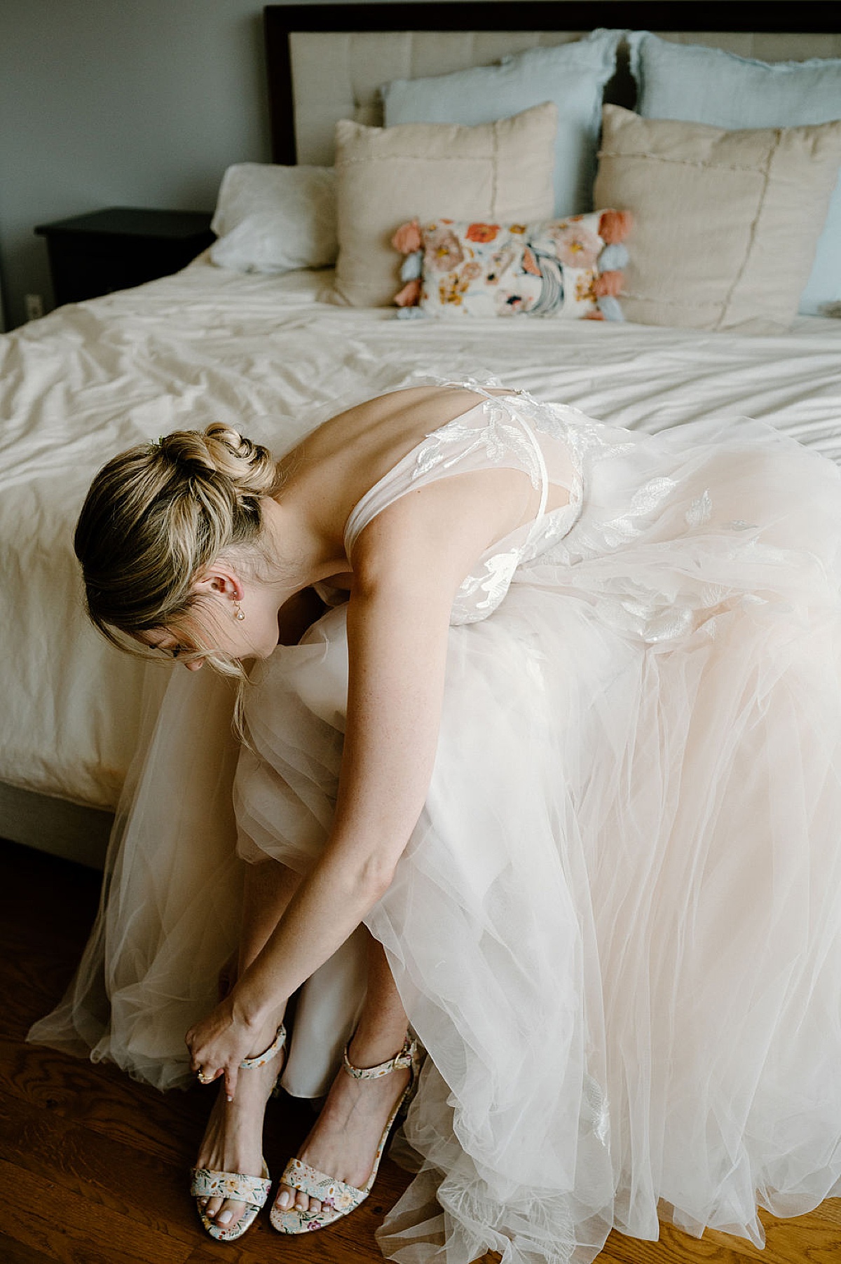 bride in romantic tulle gown fastens floral high heels before Sami and Andrew's Salvage One Summer Wedding