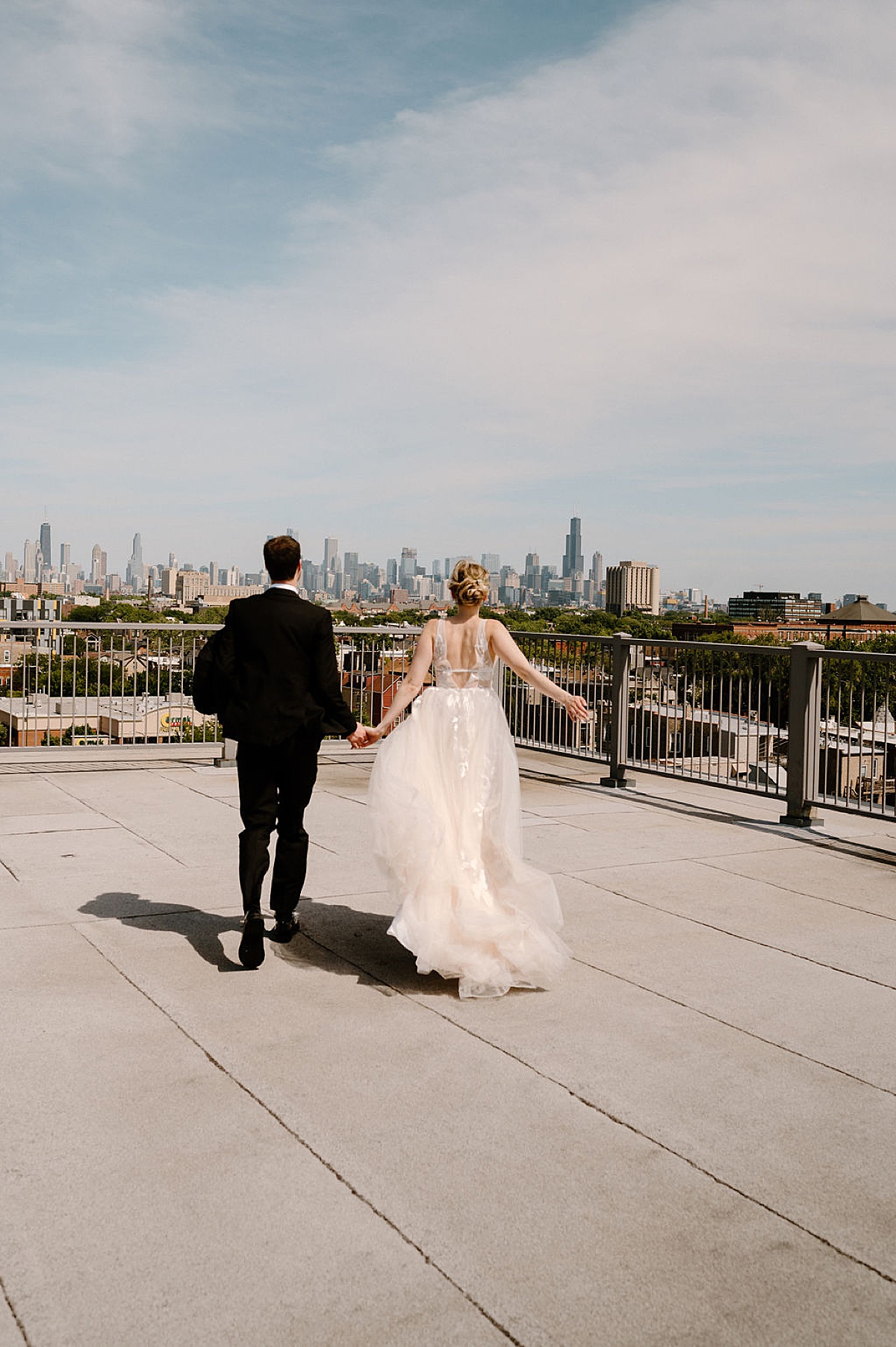 bride in elegant tulle gown and groom pose hand in hand on rooftop | chicago wedding photographer