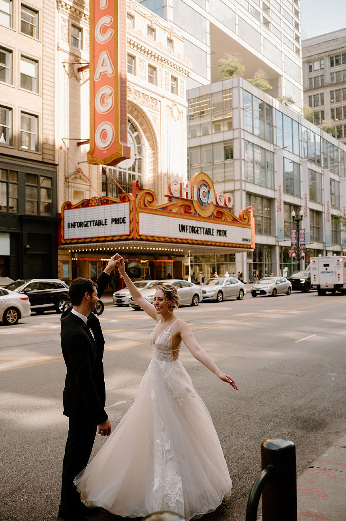 bride in romantic tulle gown twirls with groom in front of vintage theater shot by chicago wedding photographer