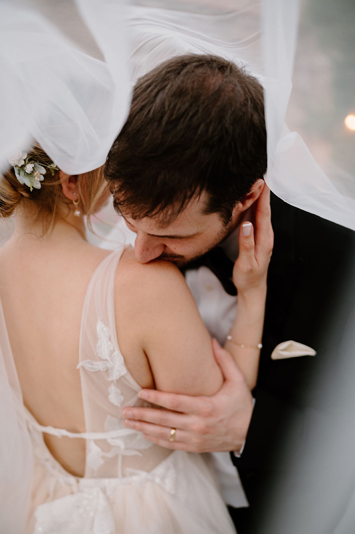 newlywed couple pose under bride's veil while groom kisses her shoulder | Indigo Lace Collective