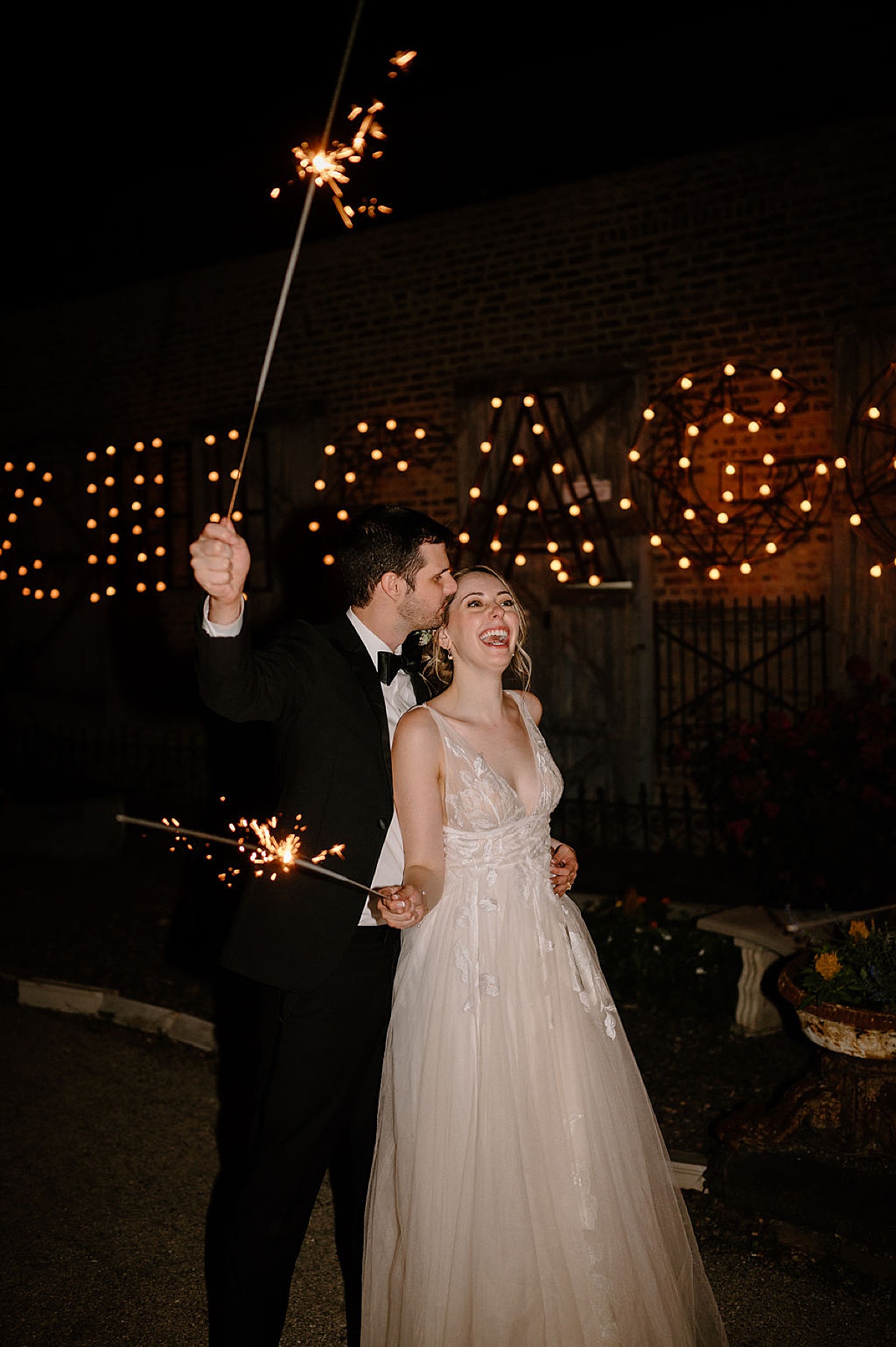 bride in romantic tulle gown and groom celebrate holding sparklers after wedding shot by Indigo Lace Collective