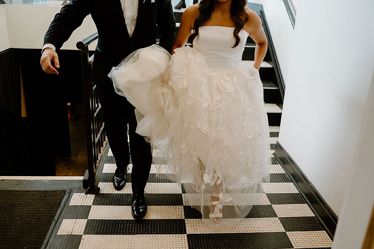 bride in couture gown and groom walk across black and white tile floor shot by Chicago wedding photographer