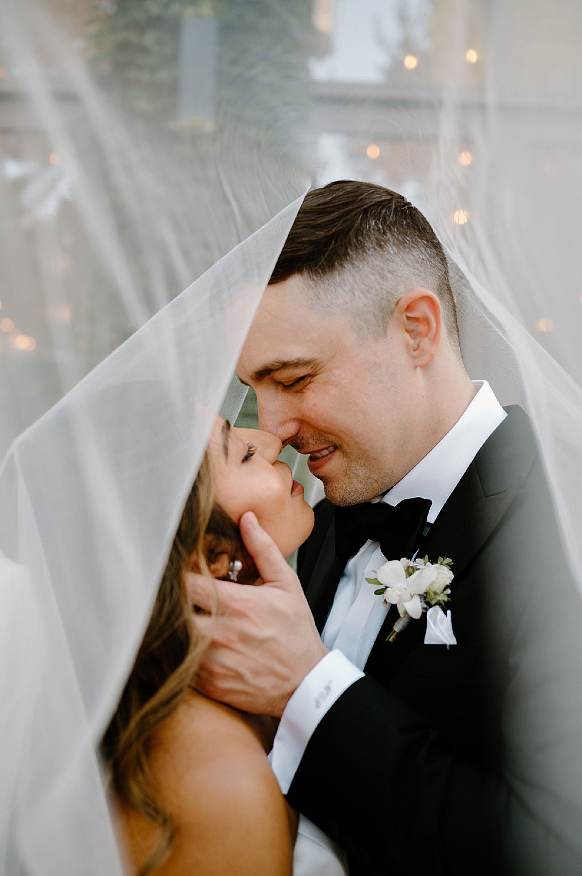 romantic bride and groom with white rose boutonniere kiss under bride's veil during shoot by Indigo Lace Collective